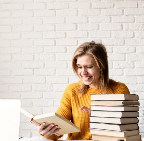 Young smiling woman in yellow sweater laughing reading a book